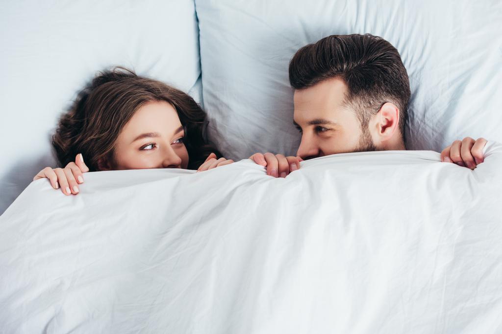 joven pareja amorosa escondido bajo manta en la cama y mirando a los ojos
 - Foto, Imagen
