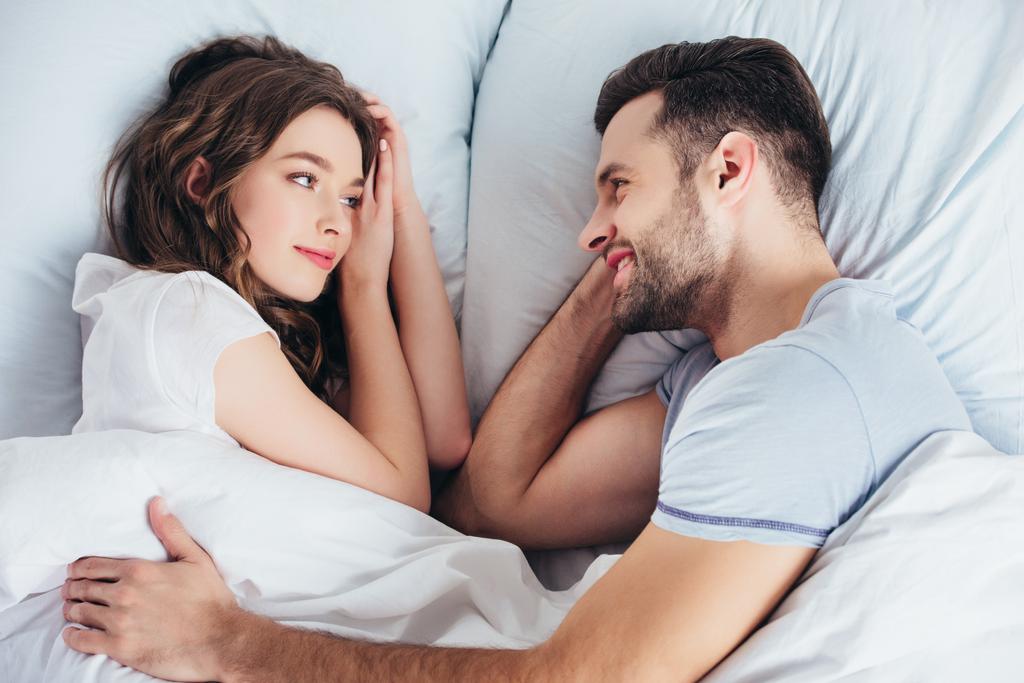 junger liebevoller Freund umarmt Freundin sanft im Bett und blickt ihr in die Augen - Foto, Bild