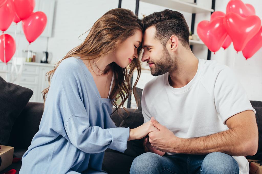young man holding hands of smiling girl while celebrating valentines day at home - Photo, Image