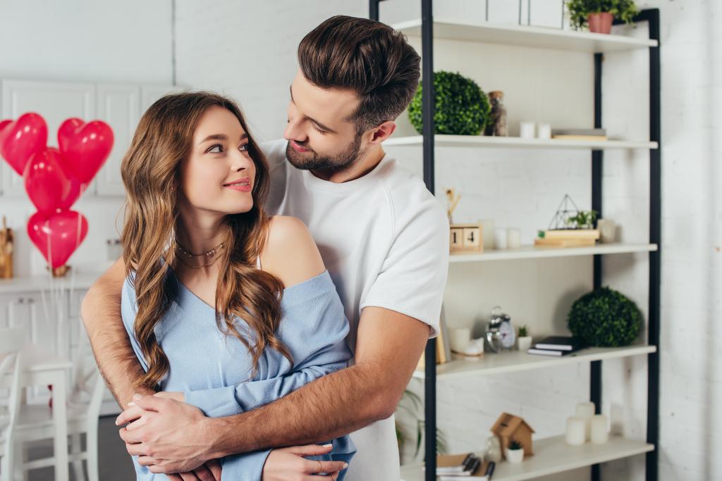 selective focus of smiling girl looking tenderly at boyfriend while man embracing girlfriend in room with st valentine day decoration  - Photo, Image