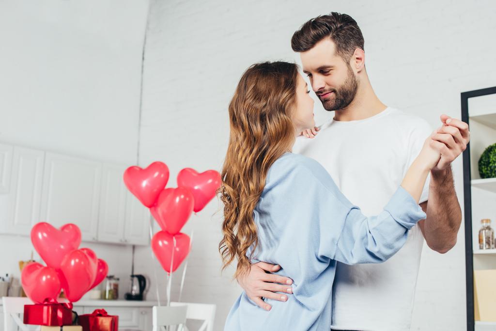 heureux couple dansant à la maison dans la chambre décorée avec des ballons en forme de coeur
  - Photo, image