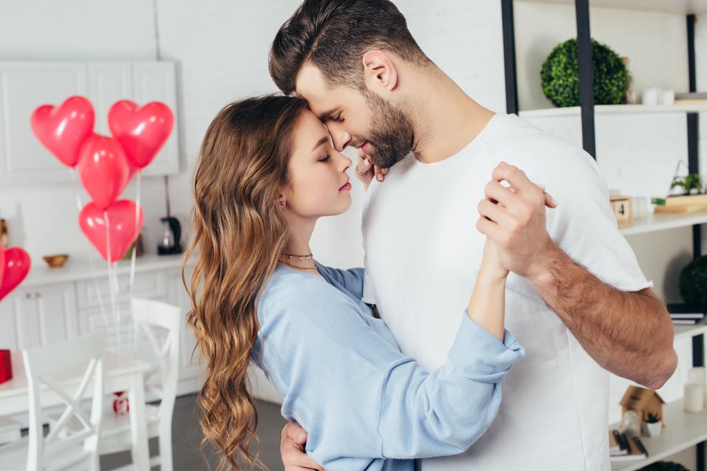 селективный фокус красивой счастливой пары, танцующей на День Святого Валентина с шарами в форме сердца на заднем плане
 - Фото, изображение