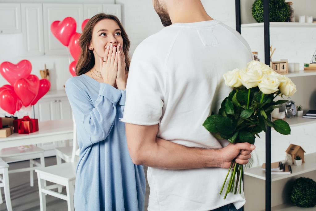 partial view of a young man holding bouquet of roses behind back while smiling girlfriend waiting for surprise - Photo, Image