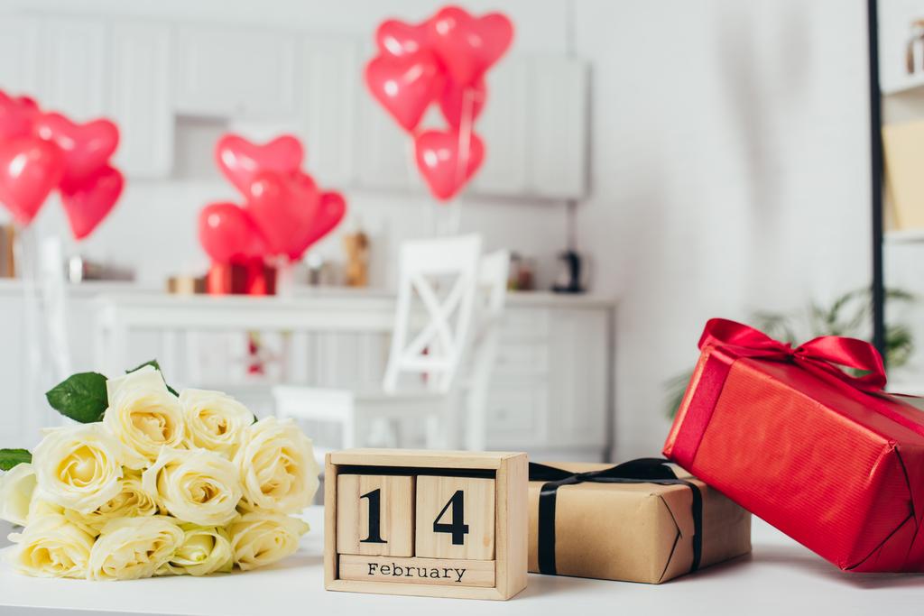 gift boxes with ribbons, roses bouquet and calendar with 14 February date on table with heart-shaped balloons on background - Photo, Image
