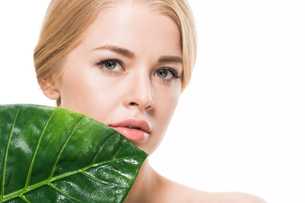 beautiful blonde girl with green tropical leaf near face looking at camera isolated on white  - Photo, Image