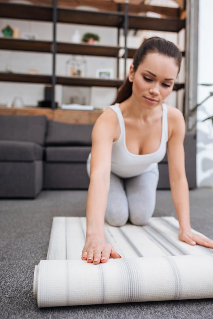 селективный фокус женщины прокатки фитнес мат для практикующих йогу дома
 - Фото, изображение
