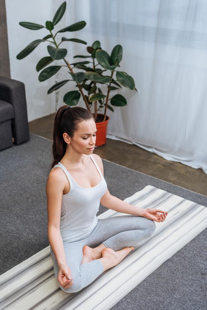 selektiver Fokus der schönen jungen Frau, die in Lotuspose sitzt und zu Hause meditiert - Foto, Bild