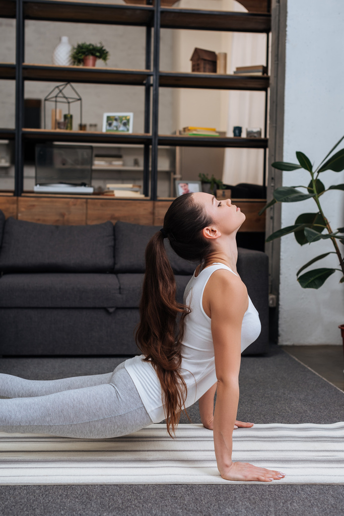 selective focus of young woman practicing cobra pose in living room at home - Photo, Image