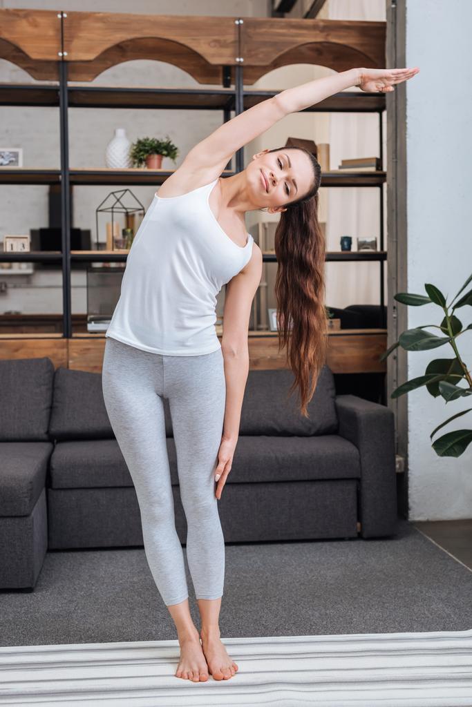 молодая женщина делает упражнения на растяжку дома в гостиной
 - Фото, изображение