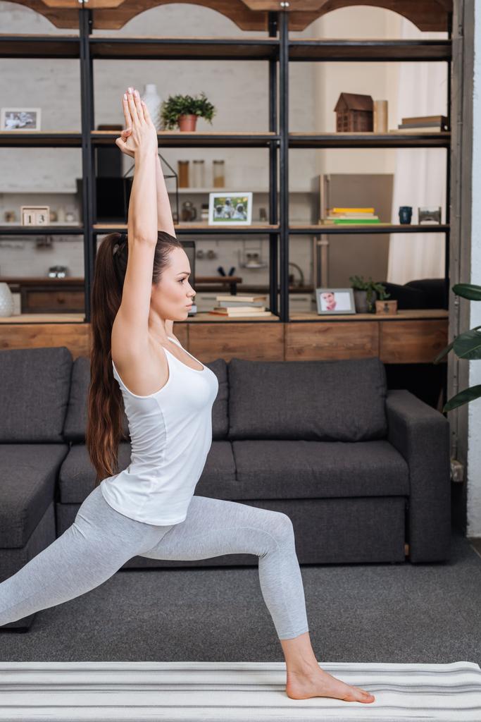 mujer joven enfocada practicando la pose guerrera en casa en la sala de estar
 - Foto, imagen