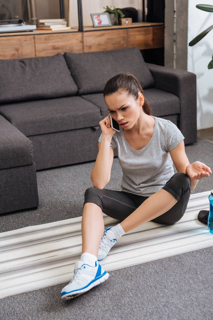 Fitness minderin üstüne oturan ve evde smartphone üzerinde konuşurken sinirli sporcumuz - Fotoğraf, Görsel