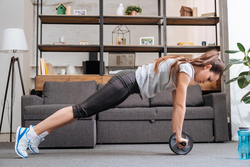 focused sportswoman exercising with ab wheel at home - Photo, Image