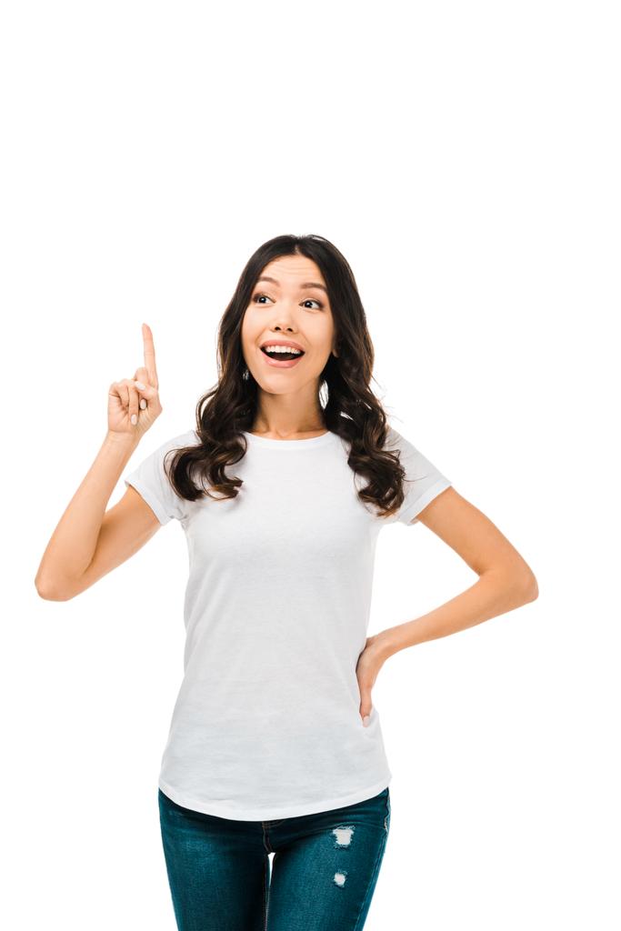 lächelnde junge Frau, die mit dem Finger nach oben zeigt und isoliert auf Weiß wegsieht - Foto, Bild