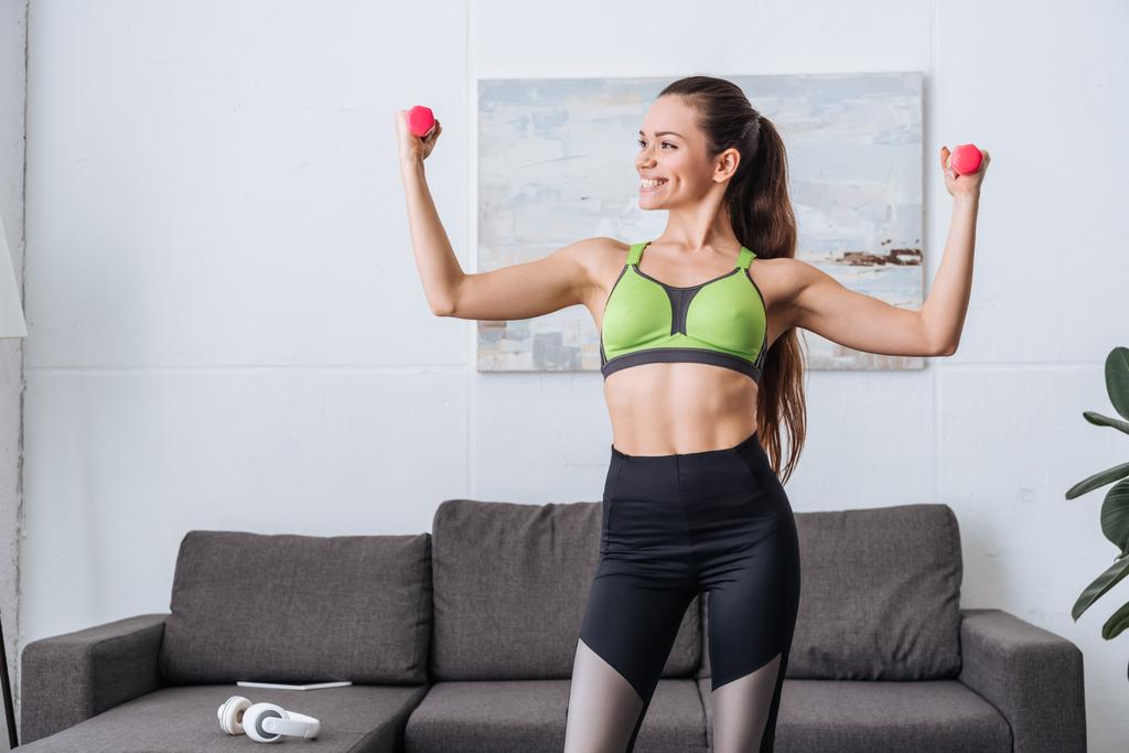 усміхнена спортсменка тренується з гантелями вдома
 - Фото, зображення