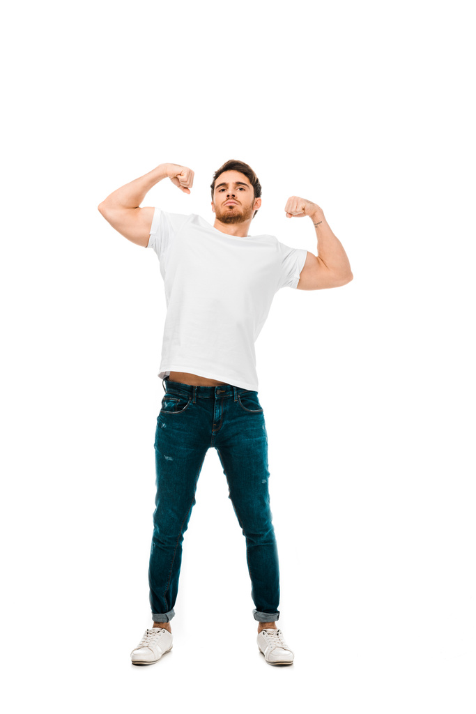 zelfverzekerde jonge man tonen biceps en kijken naar camera geïsoleerd op wit - Foto, afbeelding