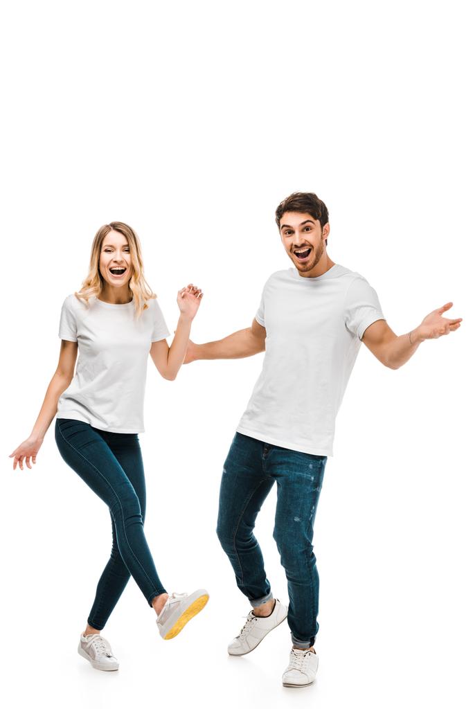 Ευτυχισμένο νεαρό ζευγάρι με λευκά μπλουζάκια να χορεύει και να χαμογελάει στην κάμερα απομονωμένο στα λευκά - Φωτογραφία, εικόνα