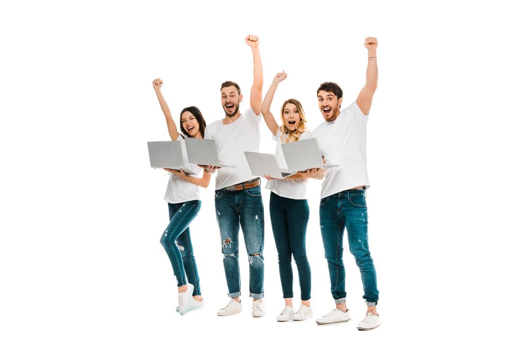 podekscytowany młodzi przyjaciele z laptopami, podnosząc ręce i uśmiecha się do kamery na białym tle - Zdjęcie, obraz