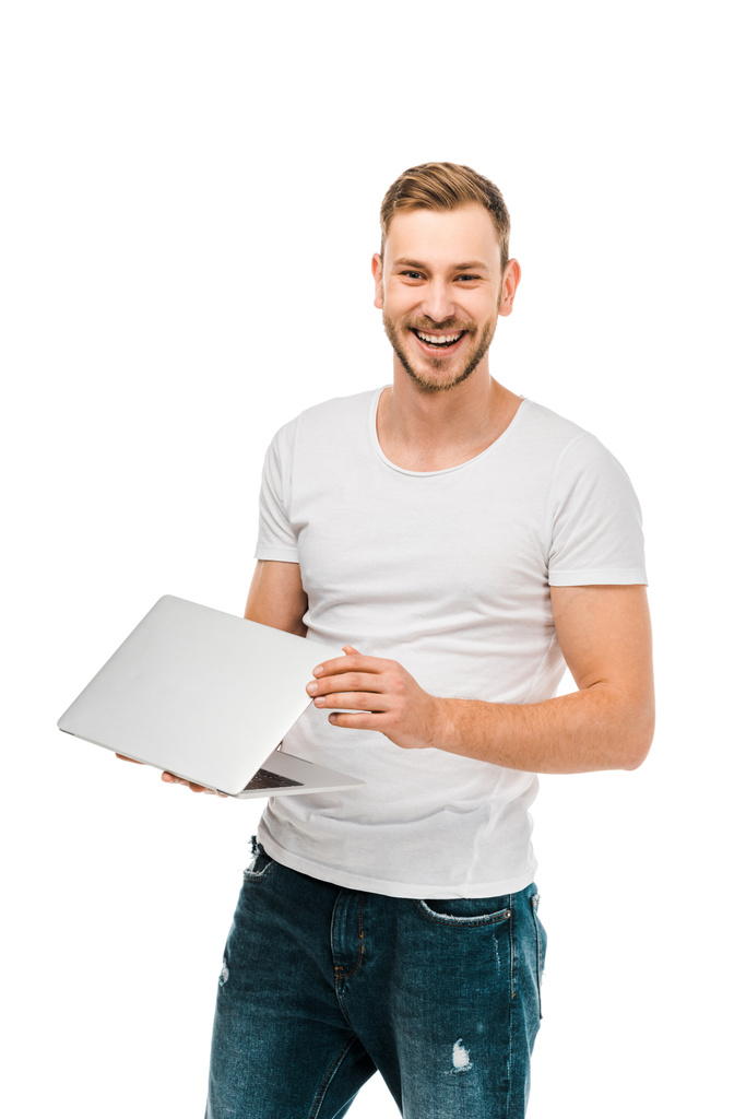 knappe jongeman holding laptop en glimlachend op camera geïsoleerd op wit - Foto, afbeelding