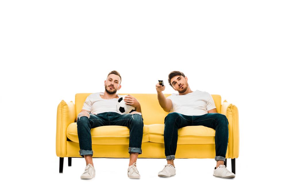 нудні чоловіки з футбольним м'ячем і пультом дистанційного керування сидять на дивані і дивитися телевізор ізольовано на білому
 - Фото, зображення