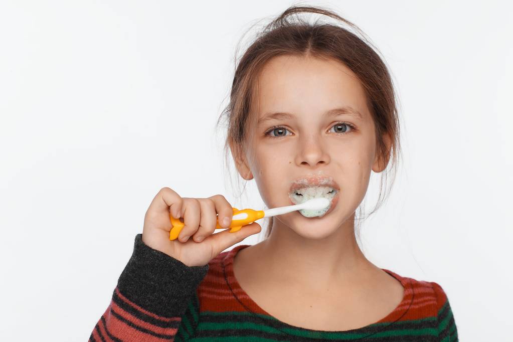 Portret van een acht-jarige meisje haar tanden met een tandenborstel borstels. Gestreepte trui - Foto, afbeelding