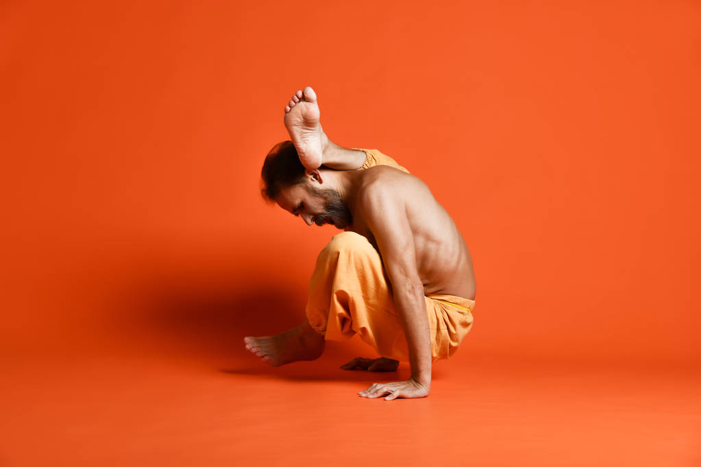 Old man practicing yoga doing stretching exercises against orange background - Photo, Image