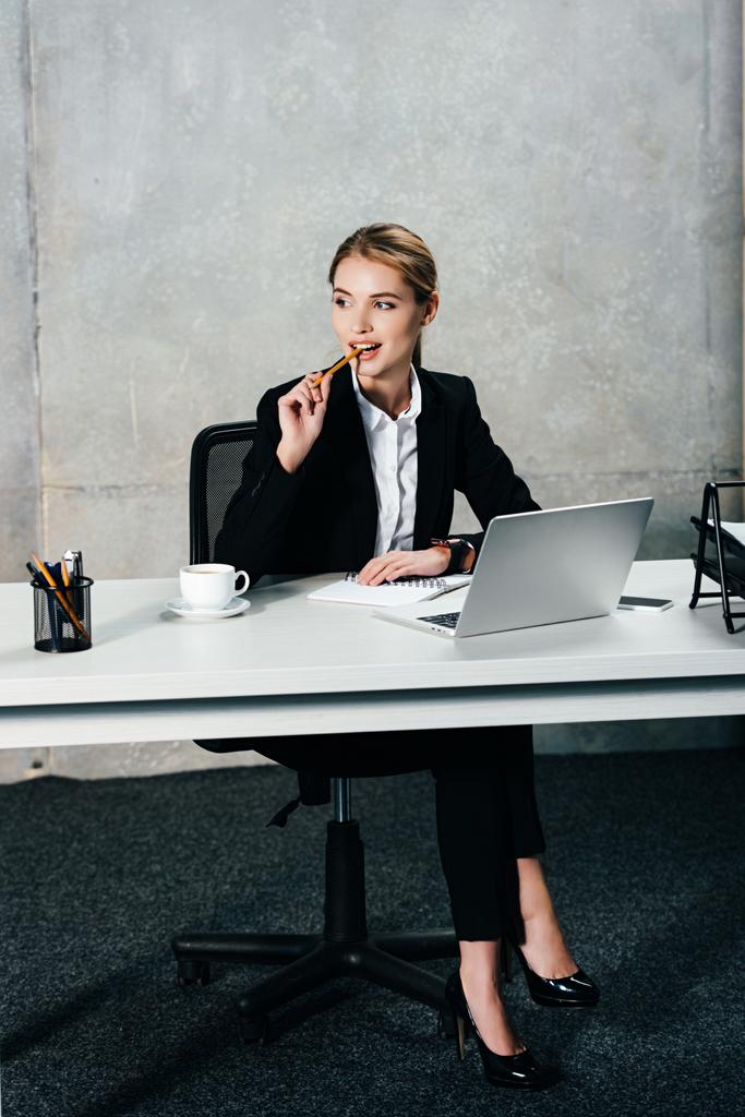 junge nachdenkliche Geschäftsfrau sitzt am Arbeitsplatz und berührt Lippen mit Bleistift - Foto, Bild