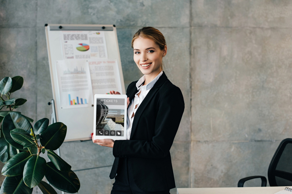 attraktive lächelnde Geschäftsfrau mit digitalem Tablet mit Tickets auf dem Bildschirm  - Foto, Bild