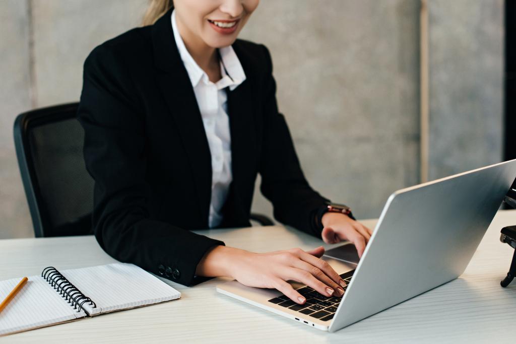 Vista recortada de la mujer de negocios sonriente usando el ordenador portátil en la oficina
 - Foto, Imagen