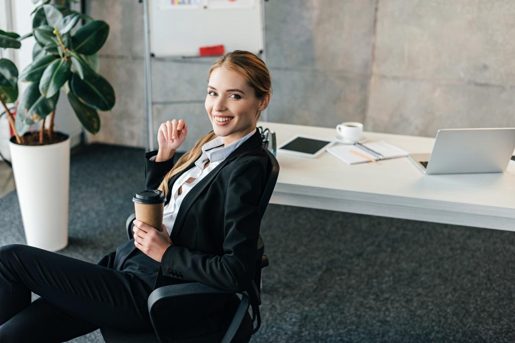 elden çıkarma fincan kahve ile sandalye üzerinde oturan genç iş kadını gülümseyen  - Fotoğraf, Görsel