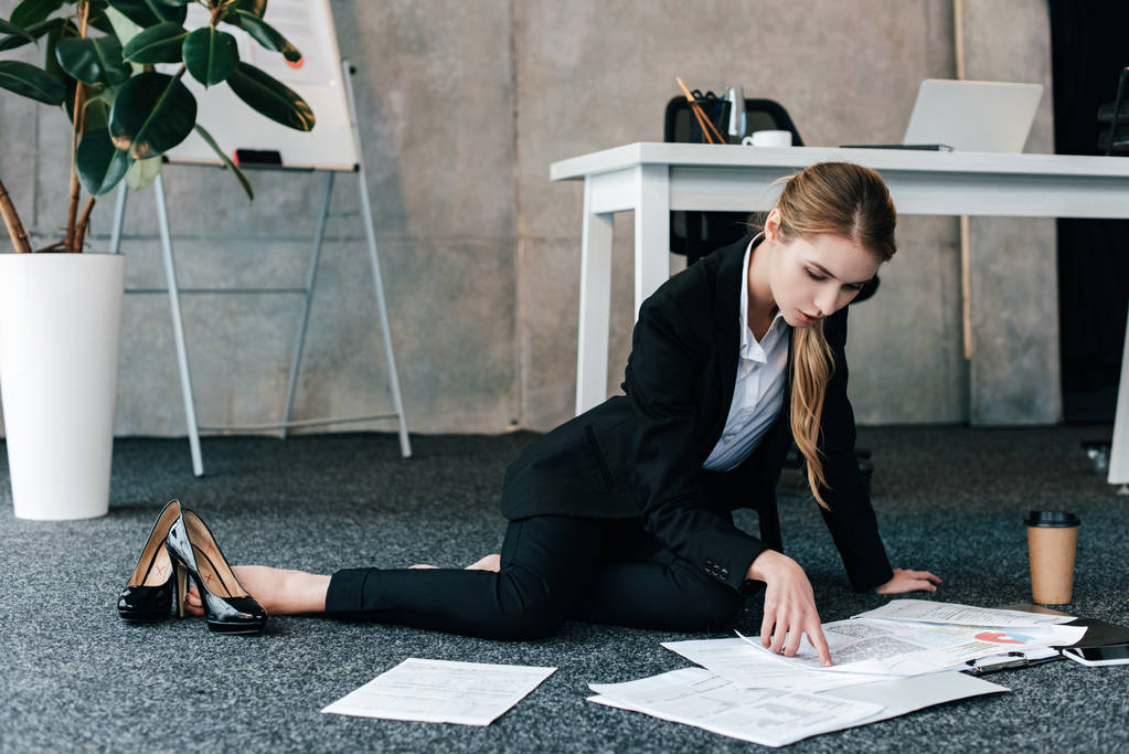 босая деловая женщина, сидящая на полу возле рабочего стола и читающая документы
 - Фото, изображение