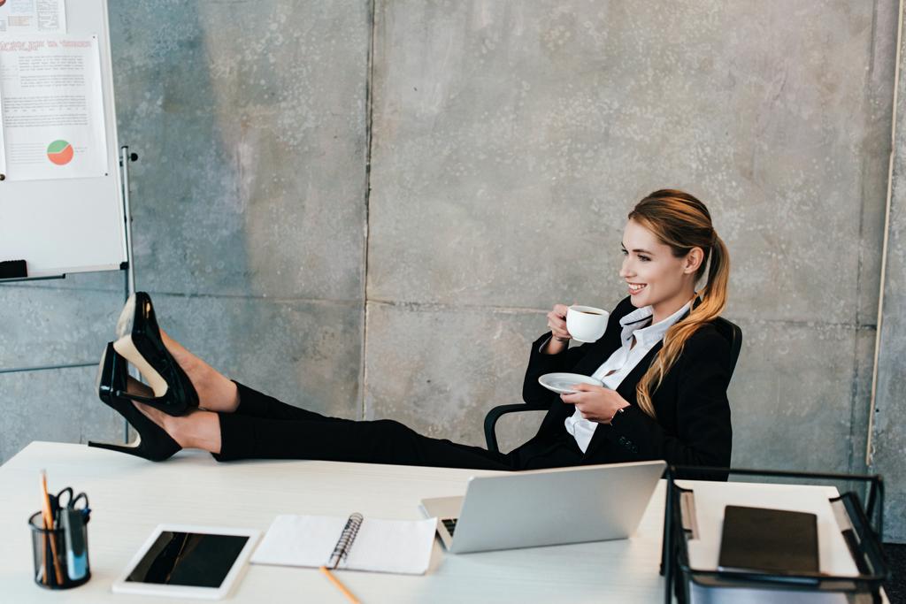 Entspannte Geschäftsfrau mit Beinen am Tisch beim Kaffeetrinken - Foto, Bild
