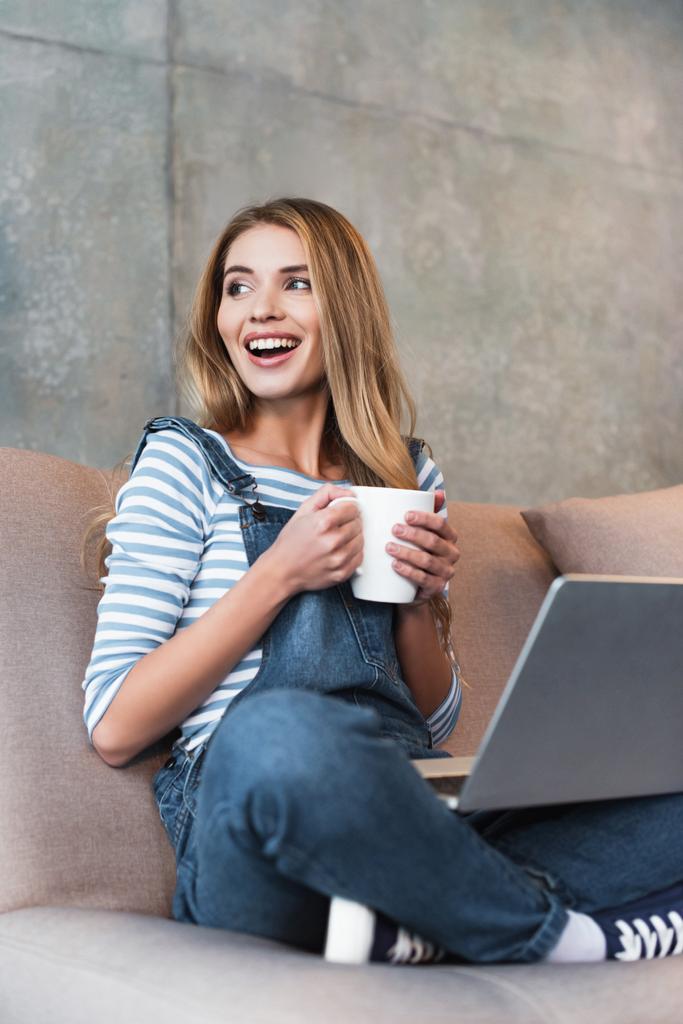 adulte femme heureuse assis avec tasse et ordinateur portable sur canapé rose
  - Photo, image