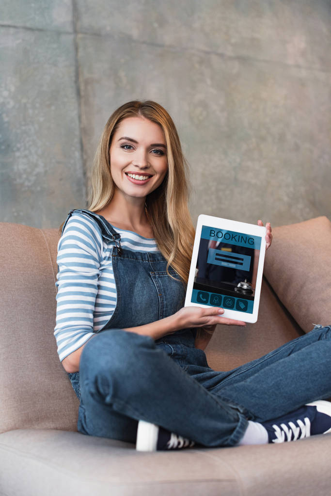 young woman sitting on sofa and showing screen with booking of digital tablet - Photo, Image