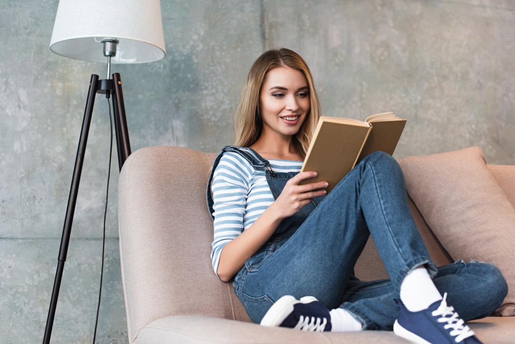 mujer joven sentada en un sofá rosa y leyendo un libro
 - Foto, Imagen