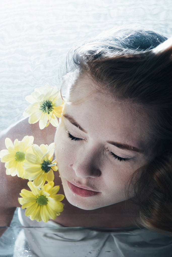 美しい女性が黄色い花を持つ水中ポーズのクローズ アップ - 写真・画像