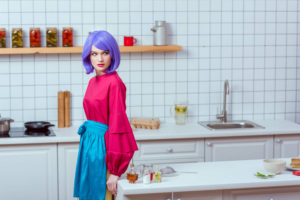 selective focus of beautiful housewife with purple hair and colorful clothes posing in kitchen with copy space - Photo, Image