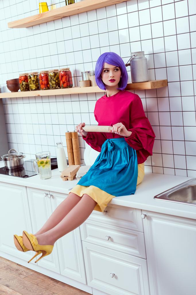 домохозяйка с фиолетовыми волосами сидит на кухонном столе со скалкой
 - Фото, изображение