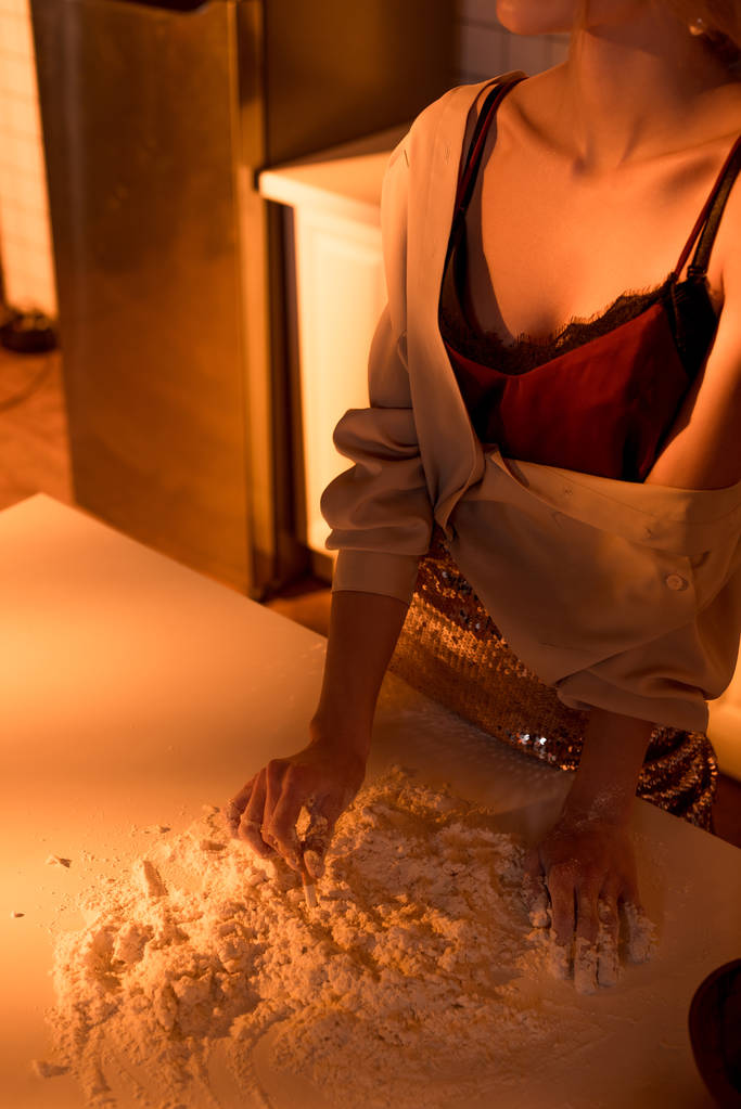 περικοπεί προβολή της γυναίκας κατάσβεση τσιγάρο στο αλεύρι, ενώ το μαγείρεμα στην κουζίνα με πορτοκαλί φως - Φωτογραφία, εικόνα