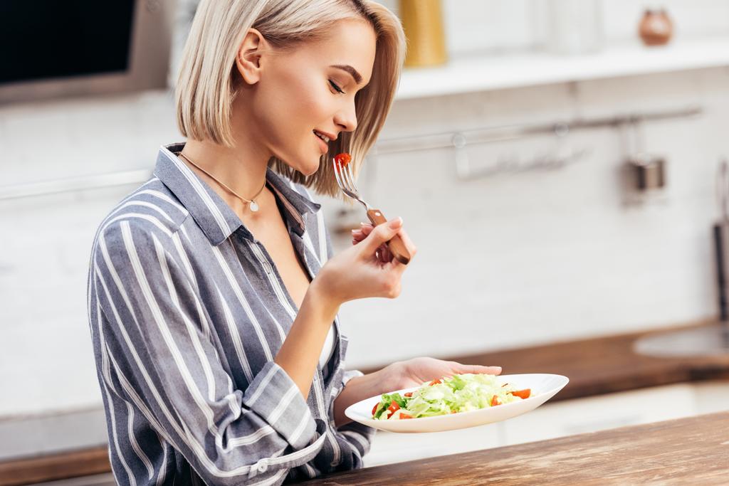 селективное внимание привлекательной женщины, держащей тарелку и обедающей
 - Фото, изображение