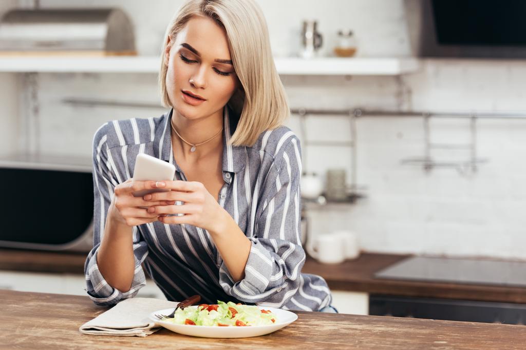 selective focus of attractive woman eating and using smartphone - Photo, Image