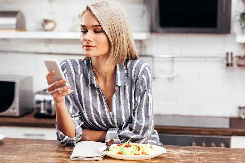 foco seletivo de mulher atraente comer e olhar para o smartphone
 - Foto, Imagem