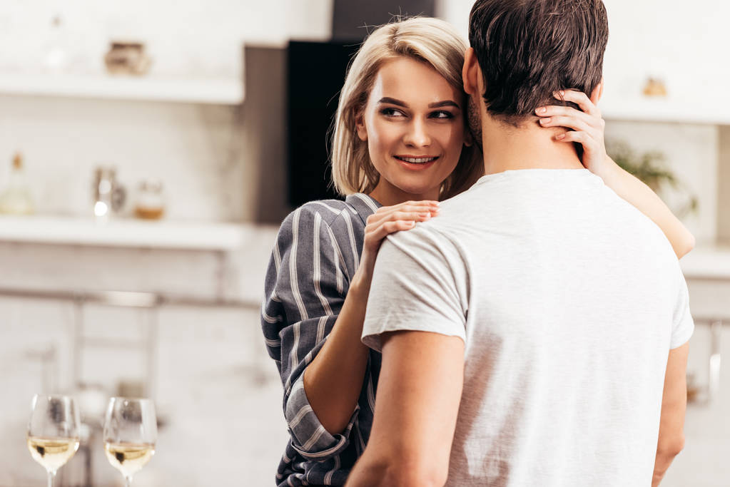 избирательный фокус бойфренда и привлекательной девушки, обнимающей и улыбающейся на кухне
 - Фото, изображение