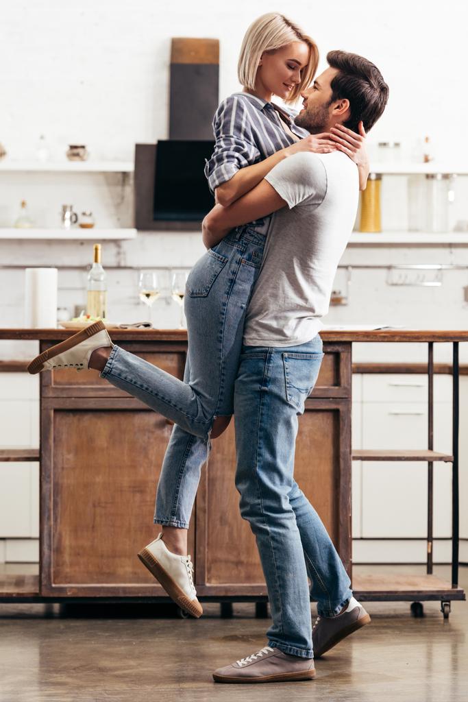 knappe vriendje en aantrekkelijke vriendin knuffelen en permanent in de keuken - Foto, afbeelding
