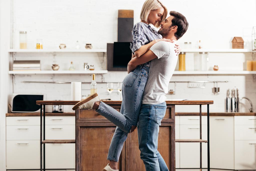 handsome boyfriend and attractive girlfriend hugging and standing in kitchen - Photo, Image