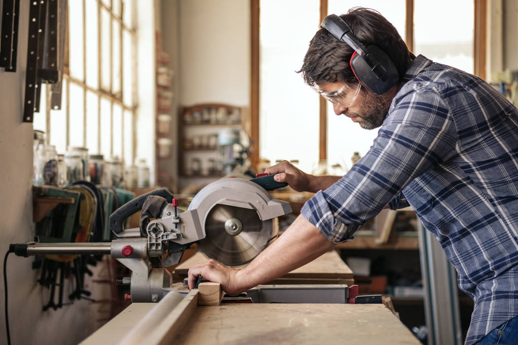Кваліфікований працівник з дерева, який використовує мітлу, щоб вирізати шматок деревини, працюючи на самоті у своїй деревообробній студії
 - Фото, зображення