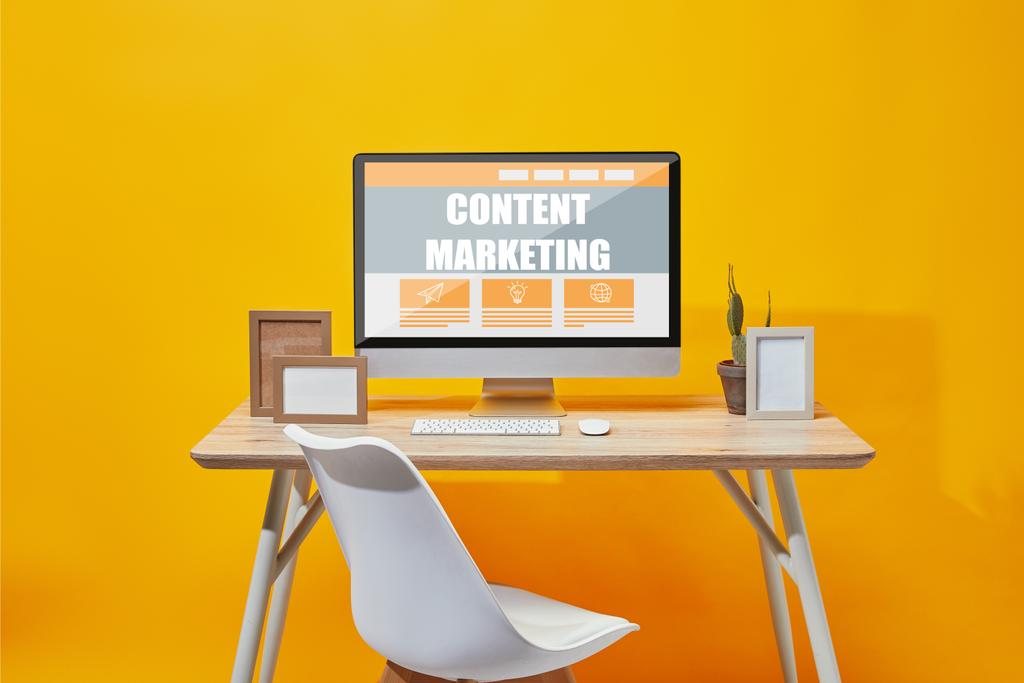 Computador com letras de marketing de conteúdo na mesa de madeira em fundo amarelo
 - Foto, Imagem