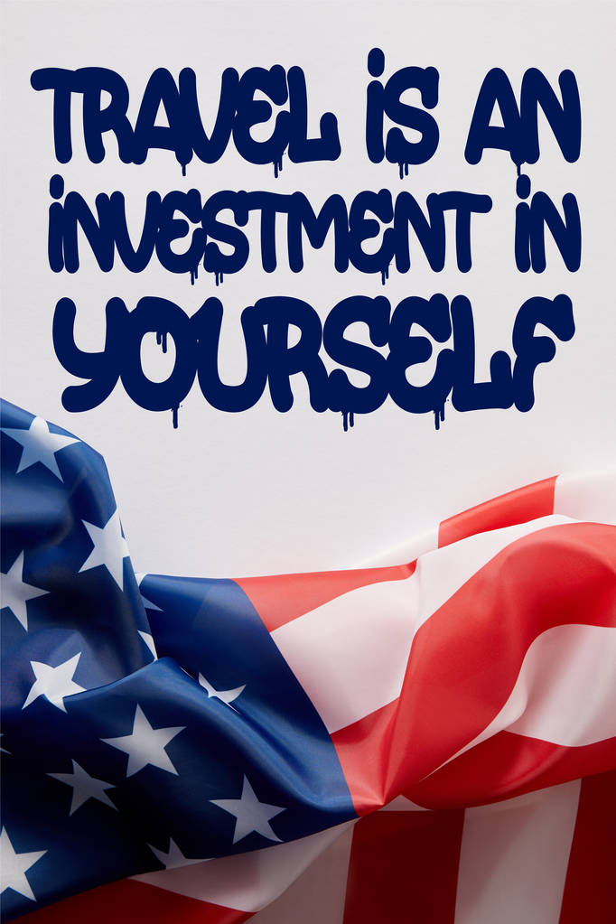 top view of united states of america flag and travel is an investment in yourself quote on white surface  - Foto, afbeelding