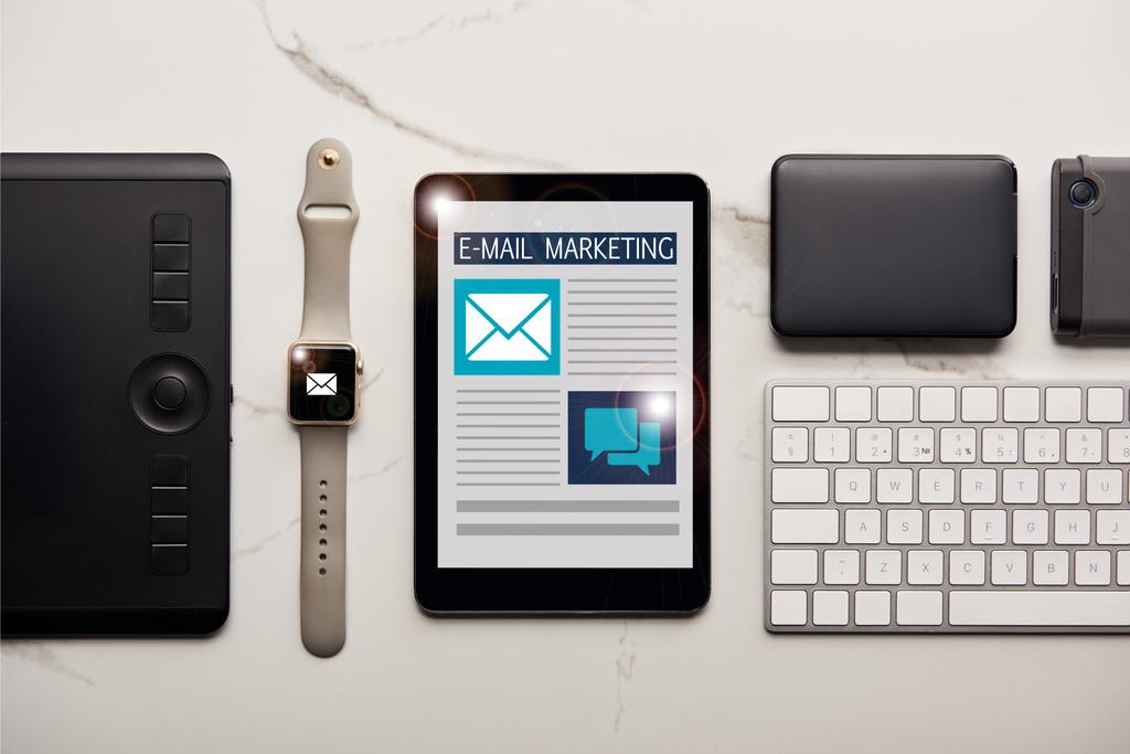 platte lay met verschillende draadloze apparaten en e-mail marketing illustratie op wit marmeren oppervlak - Foto, afbeelding