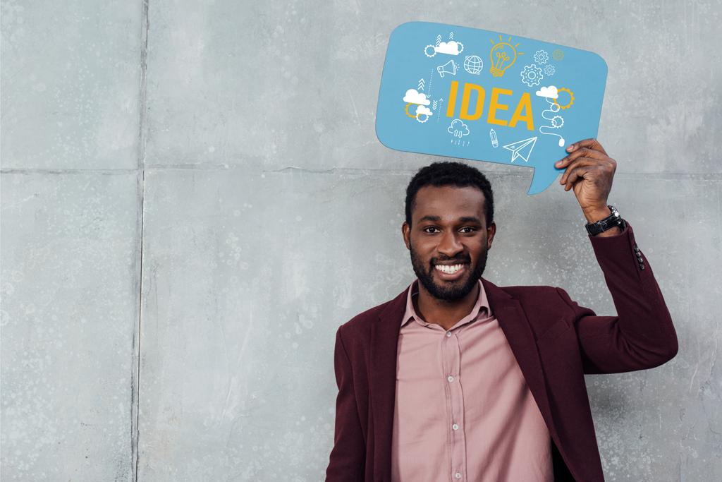 smiling african american casual businessman looking at camera and holding speech bubble with idea lettering  - Photo, Image