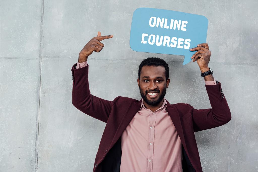 sorridente Africano americano casual empresário olhando para a câmera e apontando com o dedo para a bolha de fala com cursos on-line lettering
 - Foto, Imagem